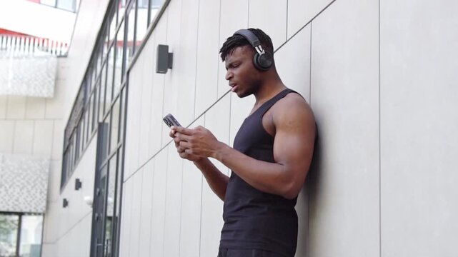 Surprised African American athletic man uses smartphone and shows facepalm on the street, muscular guy with mobile loses online and makes mistakes