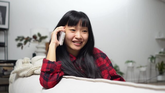 Young Asian woman sitting on the sofa and talking on the phone, girl communication on mobile phone and smiling at home
