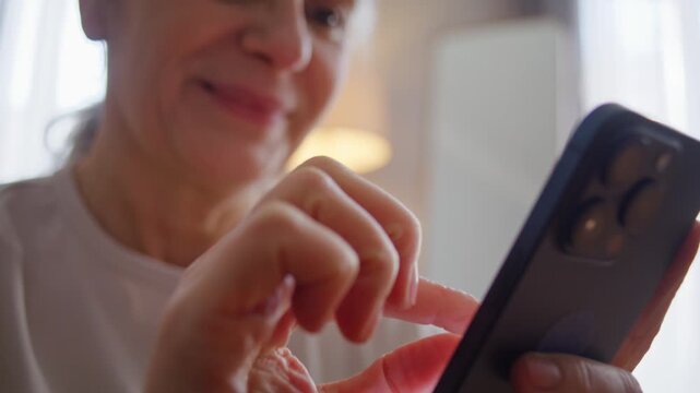 Smiling old woman scrolls internet on smartphone at home closeup