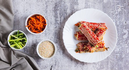 Roasted crab rolls with cucumber and carrots in sesame seeds on a plate top view web banner © elenarui