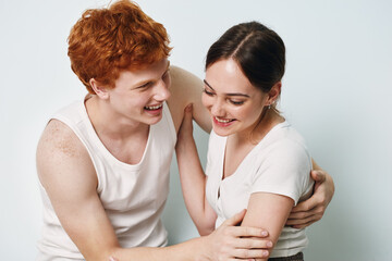 Young man and woman smiling and embracing each other in casual clothing on white background. Friendship and happiness shown with relaxed body language and joyful expressions.