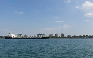 Fototapeta premium Cargo Ship Passing an Urban Waterfront Skyline