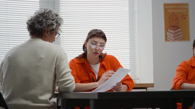 Medium shot of female teacher helping young woman inmate doing tasks and asking questions during class in prison education program, copy space