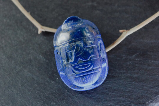 Lapis lazuli scarab beetle carving on dark slate stone with decorative dry branches, ancient amulet.