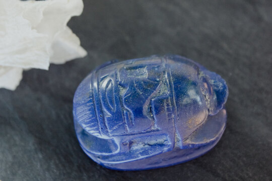 Lapis lazuli scarab figurine on dark stone with white petals, ancient Egyptian protection symbol.