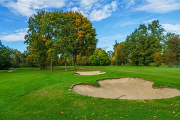 Fototapeta premium a professional golf course fairway featuring well-maintained sand traps and lush green grass. Beautiful autumn foliage on surrounding trees creates a peaceful outdoor sports atmosphere