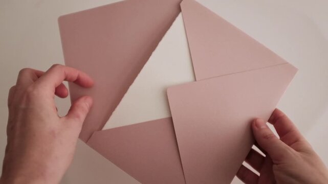 Elegant wedding invitation suite featuring a soft blush pink velvet ribbon tied in a bow on luxury textured pastel pink paper envelope. Close-up slow-motion detail video of bridal stationery.