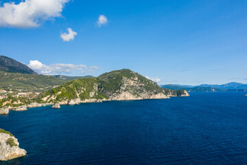 Naklejka premium Wide view of the deep blue Ionian Sea meeting rugged, forested cliffs along the coastline near Parga in Epirus, Greece. The Mediterranean landscape features clear sky, dramatic rock formations, and