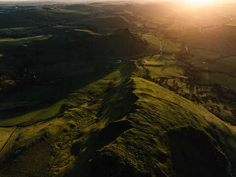 Aerial view of Mam Tor and the Great Ridge basked in the golden light of the setting sun, casting long shadows across the verdant hills, Peak District, Peak District National Park, United Kingdom.