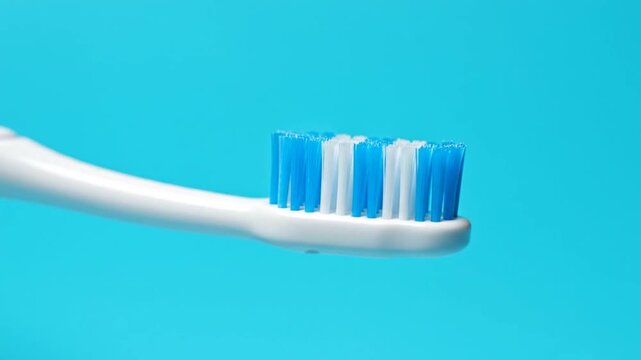 Close-up of a white toothbrush with blue bristles against a vibrant blue background.