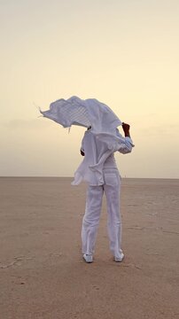 Woman waves scarf on vast salt lake at sunrise in serene Sahara desert environment, vertical video