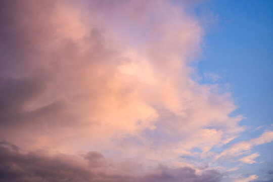 Delicate peach and lavender clouds float across a bright blue sky, creating a serene and airy atmosphere with gentle light and subtle color transitions.