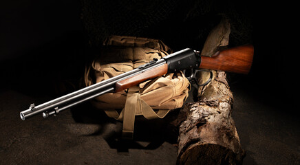 Lever action rifle with wood stock resting on a log and pack