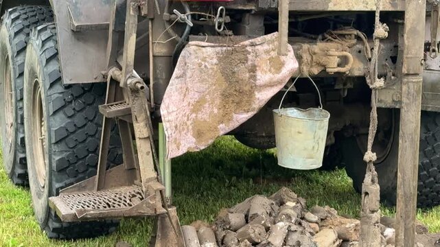 Drilling rig extracting soil cores in grassy field, truck mounted rotary rig creating borehole while driller operates controls, core tray with cylindrical samples laid on grass, geologist.