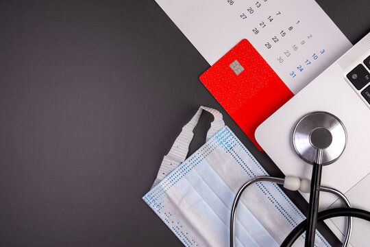 Flat lay of stethoscope, laptop, red credit card and calendar on dark background with copy space, medical insurance concept