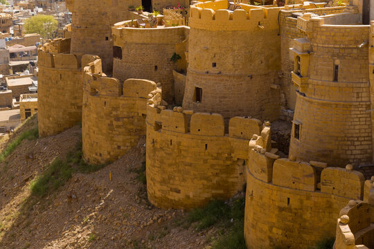 Robust golden sandstone bastions form a curving defensive wall at Jaisalmer Fort, illuminated by warm sunlight and overlooking the city below.