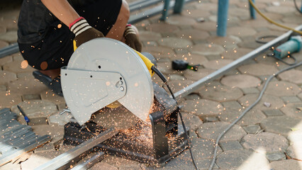 Skilled worker cuts steel pipe using chop saw on paved surface, generating bright flying sparks during outdoor metal fabrication project at residential construction site.