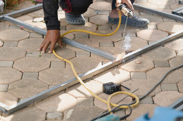 Close view skilled manual worker welding steel bars on paved floor outdoors, creating hot sparks smoke while fabricating metal frame construction maintenance.