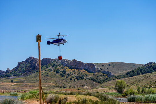 Firefighting helicopter filling water with bambi bucket from a lake