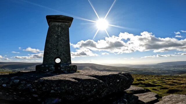 Stone viewpoint marker atop rocky moorland with bright sun