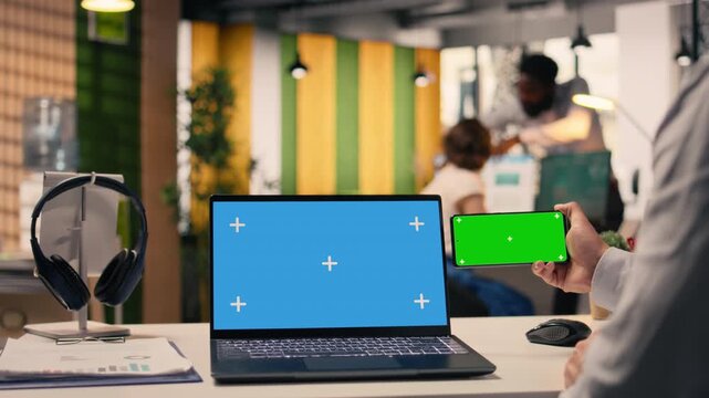 Chroma key on phone and blue screen on laptop at desk with businessman, data analysis and productivity ensuring business research and development. Multinational company tasks.