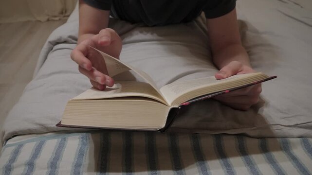 Male hands reading book. Closeup of turning page. Intimate scene of reading with gentle lamp lighting. Detailed depiction of teenager gently flipping through wellloved book in cozy setting