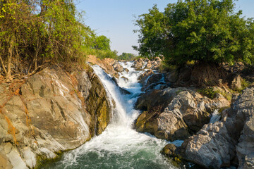 Daylight reveals energetic waterfalls tumbling over rugged rocks and surrounded by lush green trees at Li Phi Falls, also known as Tat Somphamit Waterfalls, in Champasak Province, southern Laos. The