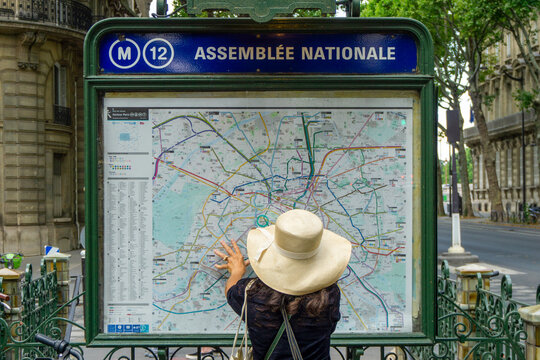 Paris, France - July 13, 2019: Woman with Sun Hat Checking Paris Metro Network Map at Assemblee Nationale Station Entrance
