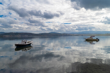 With calm, reflective sea and boats and cloudy sky