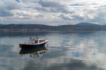 With calm, reflective sea and boats and cloudy sky