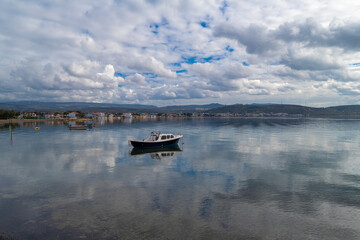 With calm, reflective sea and boats and cloudy sky