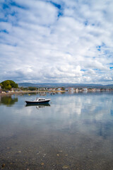 With calm, reflective sea and boats and cloudy sky