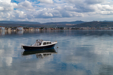 With calm, reflective sea and boats and cloudy sky