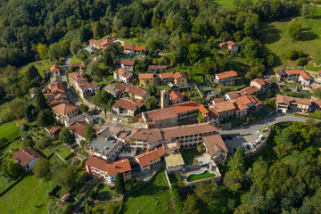 Aerial perspective of Ceresito in Piedmont, Italy, featuring clustered houses with terracotta roofs surrounded by green hills and dense woodland. The tranquil rural settlement is framed by open