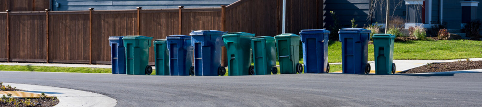 Residential garbage day, row of garbage and recycle rolling bins lined up at street curb on a sunny winter day
