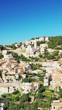 Aerial view of the picturesque hillside village of Corbara with traditional Mediterranean houses and lush greenery under a clear blue sky in Corsica, France.