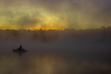 predawn early morning fog over lake with a fisherman in a boat silhouette
