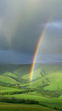 Rainbow over rolling green hills after rain.