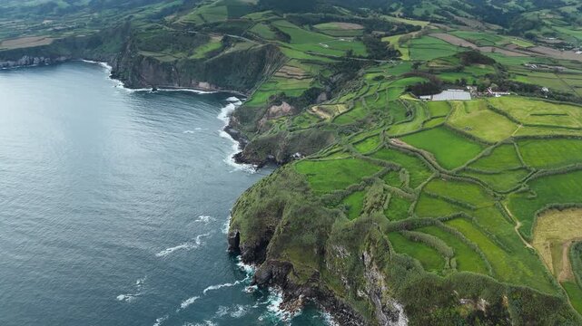 Geometric patchwork fields meeting rugged Atlantic coastline on volcanic island in Azores. Aerial view