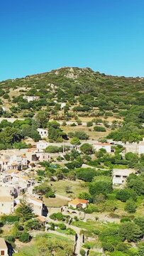 Scenic aerial shot of Corbara village nestled among green hills under a clear blue sky in Corsica, France.