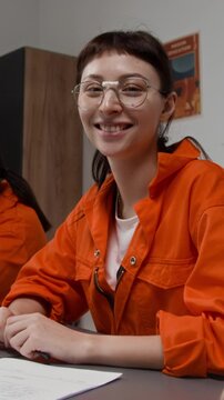 Vertical shot of smiling female inmate looking at camera while sitting at table with group of people during class in correctional facility