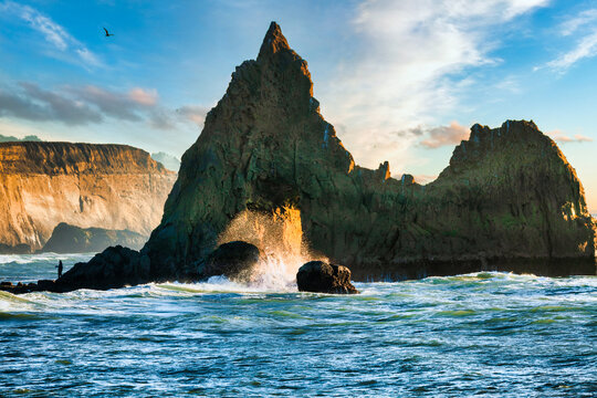 Dramatic sea stacks and rugged rock formations at Martins Beach on the California coast, with ocean waves, warm sunset light, and colorful sky over the Pacific Ocean