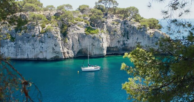 Sailing boat entering a narrow calanque near Cassis, France. Clear blue water, rocky cliffs and protected Mediterranean coastline