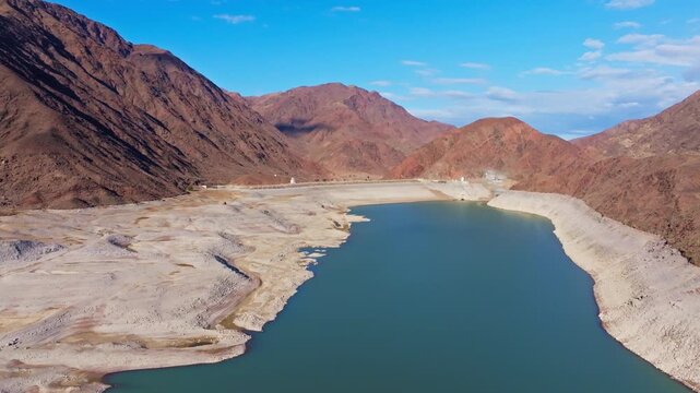 Aerial view captures tranquil Orto Tokoy reservoir with dam surrounded by majestic mountains in Kyrgyzstan.