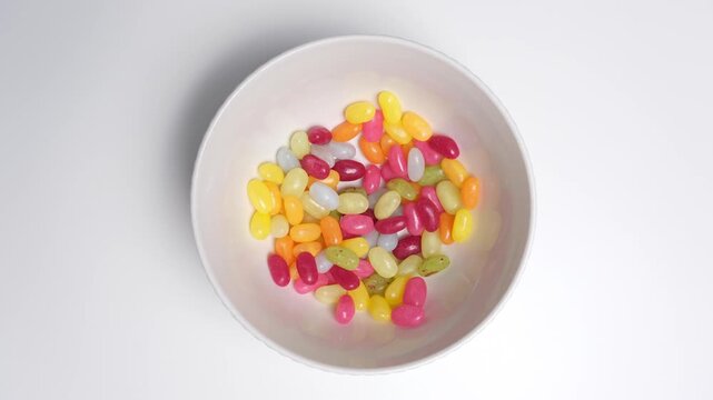 Stop motion of colorful jelly beans constantly changing positions in a white bowl, top view, minimal flat lay, random movement concept. Stop motion food background