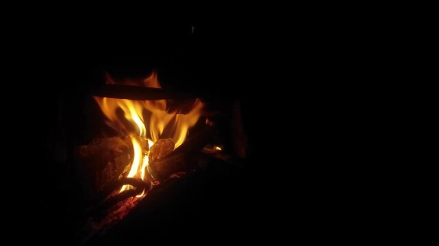 Cinematic close-up shot of bright orange flames flickering and burning wooden branches in the dark