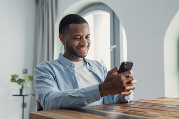 Smiling cheerful African American man looking at phone screen, reading good news in message, having...