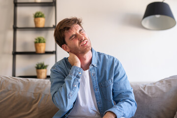 Fototapeta premium Upset tired young man feeling pain massaging stiff neck rubbing tensed muscles to relieve back ache joint shoulder discomfort after long sedentary work in incorrect posture, fibromyalgia concept