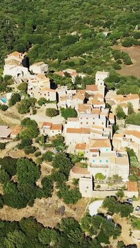 Scenic aerial shot of the traditional hilltop village of Pigna surrounded by lush greenery in Corsica, France. Picturesque Mediterranean architecture with terracotta rooftops and stone houses.