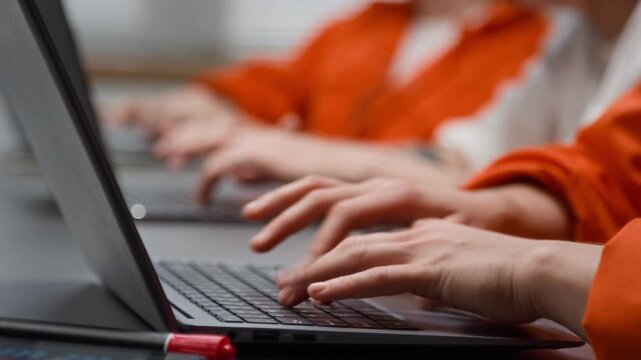 Side view close up shot of group of unrecognizable young women as female inmates using laptops and typing on keyboards swiftly during computer programming class